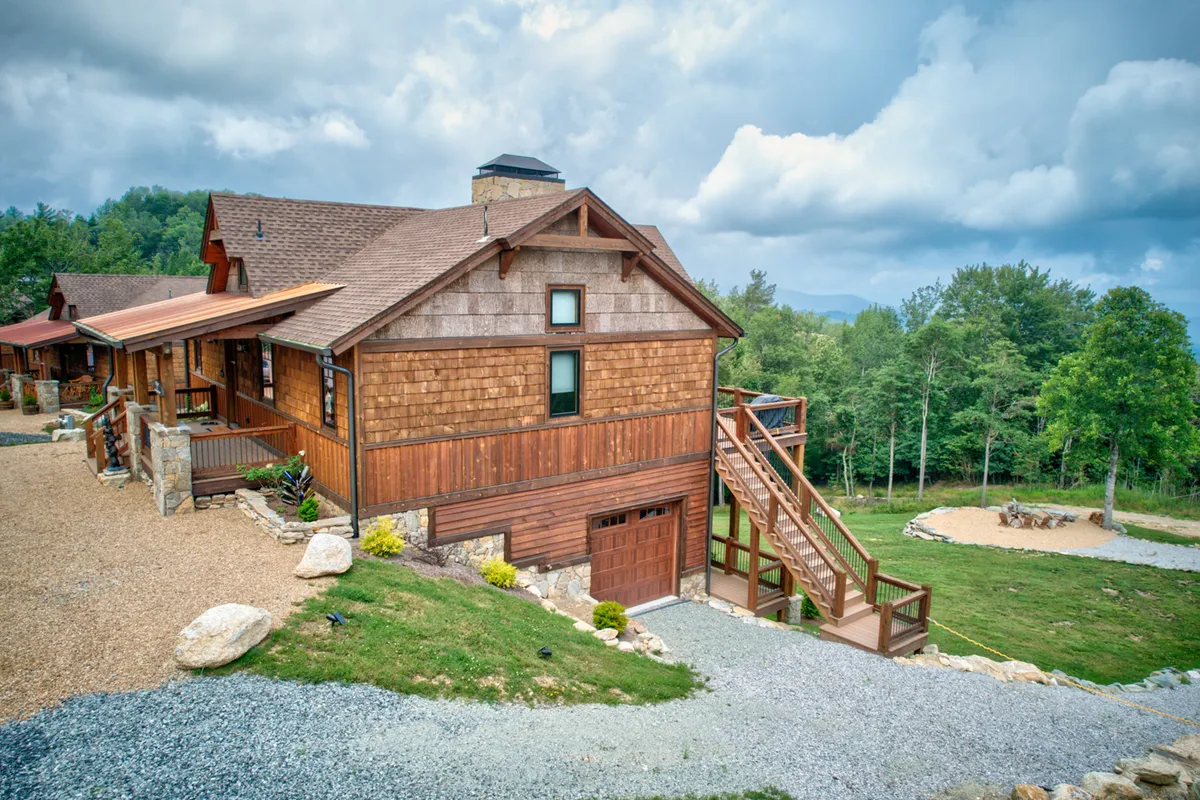 A cozy wooden exterior with a staircase leads to the home, set against a manicured yard with large boulders and mountain scenery in the background. The space feels inviting for outdoor gatherings and provides visual cues of nearby trails and communal activities.