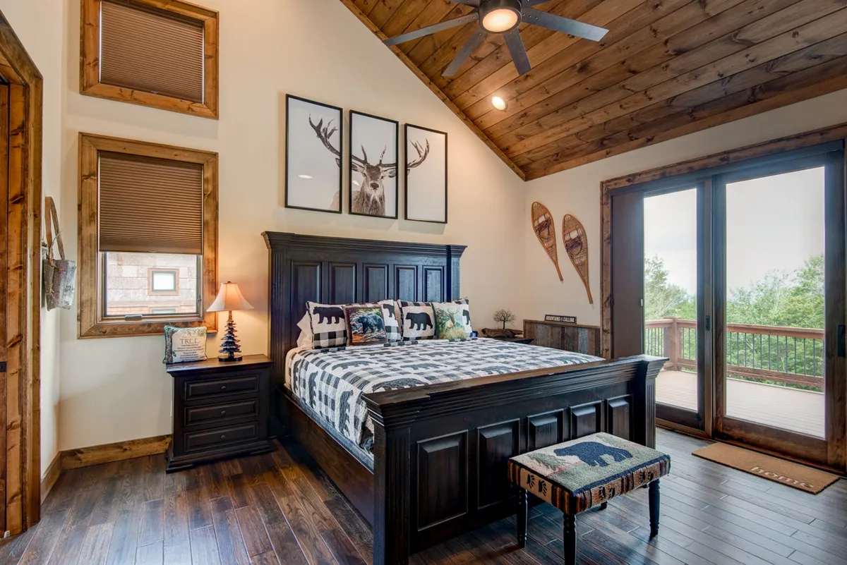 An inviting king bedroom with a sturdy wooden bed frame, decorative pillows, nature-themed artwork, and a sliding glass door that lets in sunlight and offers peaceful views. The tranquil mood and ample light create a soothing atmosphere for relaxation or quiet mornings.