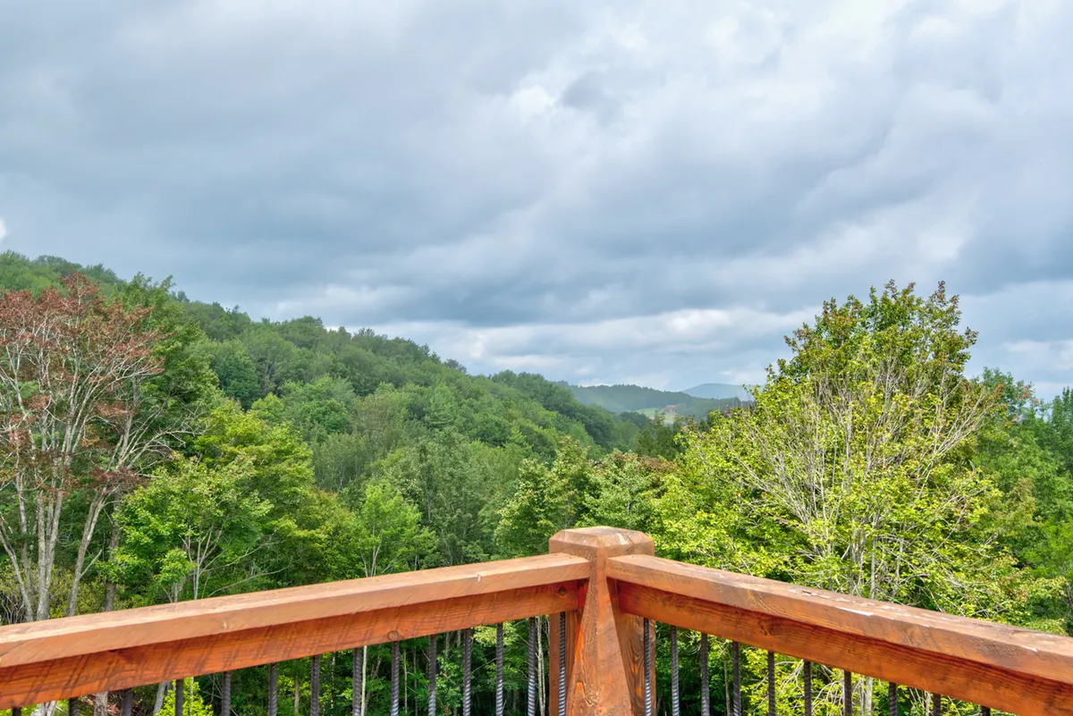 A panoramic view of the mountain range framed by lush greenery and a rustic wooden railing. The scene is tranquil, inviting moments of awe as you take in the vastness of the landscape—perfect for sunrise coffee, sunset wine, or stargazing sessions.