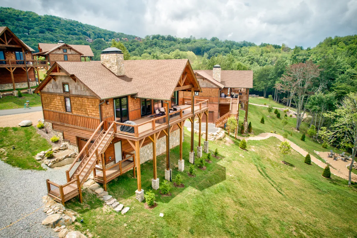This image showcases a wooden deck with comfortable seating set atop a stone foundation, surrounded by lush greenery and framed by a striking mountain backdrop. The tranquil outdoor setting invites relaxation and social engagement, with space for gatherings and the opportunity to appreciate beautiful sunset and stargazing views.